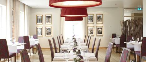 A long dining table with chairs, red pendant lights, and framed pictures on the walls.