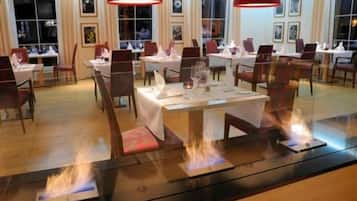 Un restaurante con mesas dispuestas para comer, iluminación roja en el techo y una chimenea central.