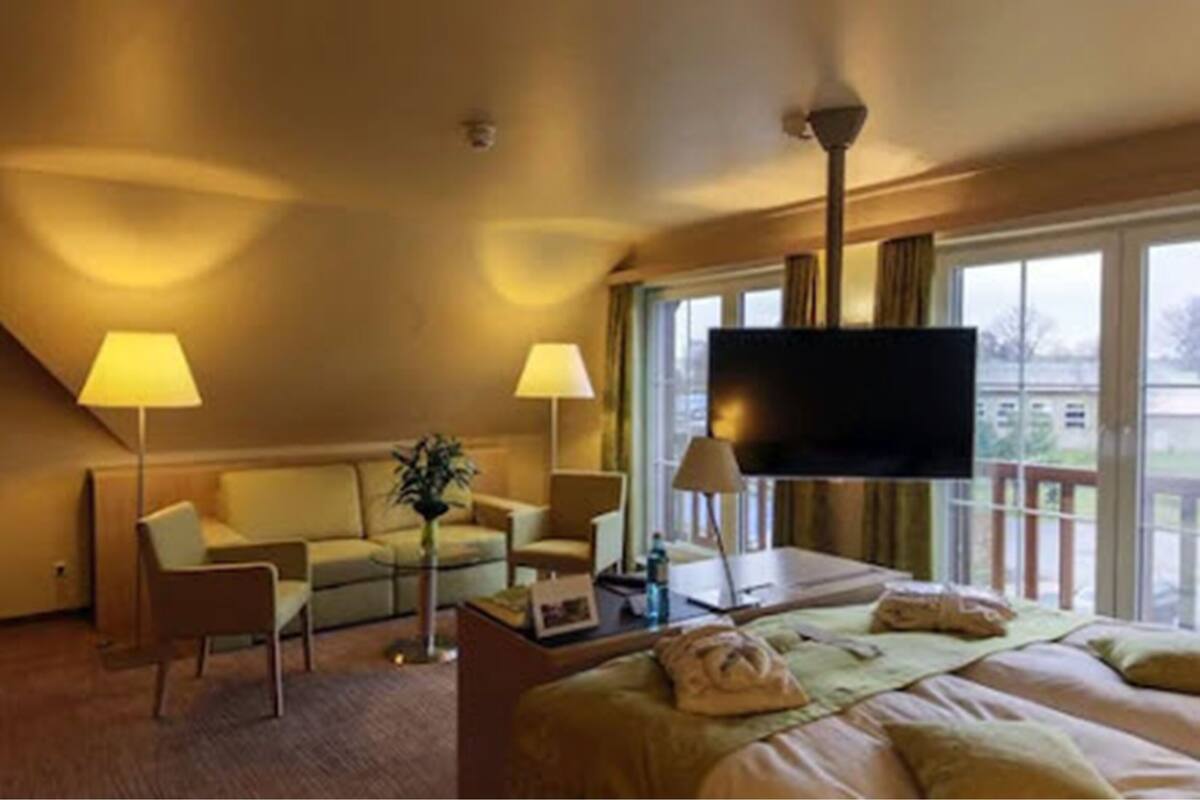 A hotel room with a bed, a sofa, a TV, and a balcony with a view.