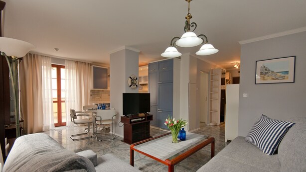 Una sala de estar con sofá, mesa de centro y televisor. Hay un comedor con una silla y una mesa.