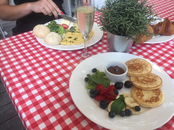 A table with a red and white checkered tablecloth, a plate of pancakes with berries and chocolate sauce, a glass of champagne, and a potted plant.