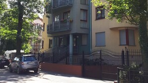 Un edificio residencial de varios pisos con balcones, una entrada con reja y un automóvil estacionado.