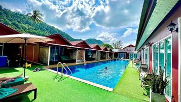Zona de piscina con sillas de descanso, un trampolín y vistas a montañas.