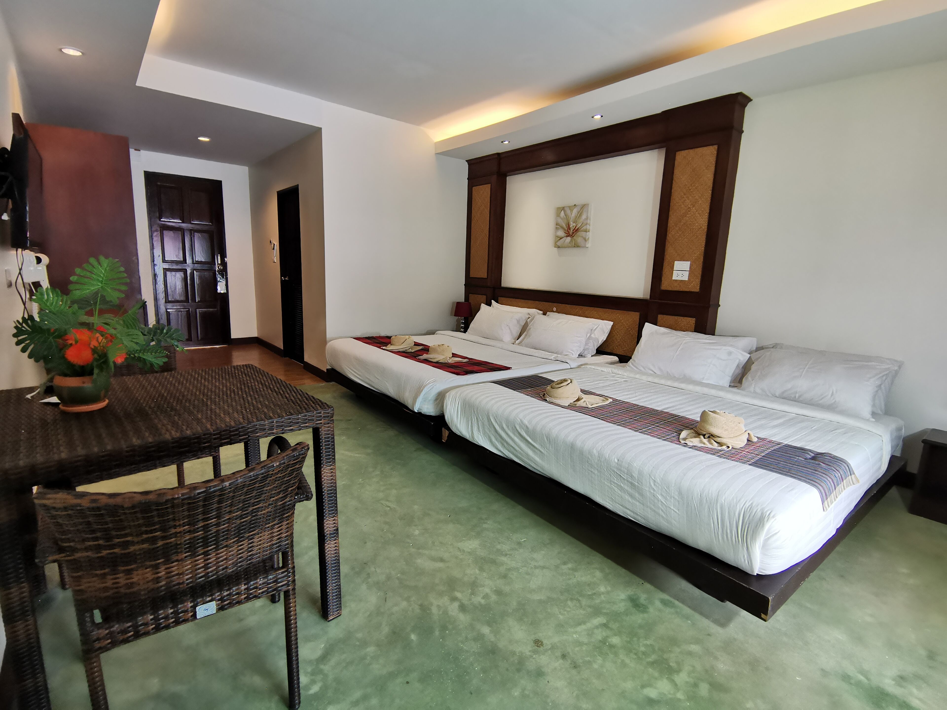 A hotel room with two beds, a dining area with a table and chairs, and a potted plant.