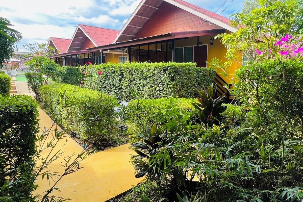A row of bungalows with red roofs, surrounded by well-maintained greenery and a paved walkway.