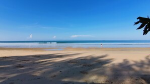 Een strand met heldere lucht, rustige golven en een eiland in de verte.