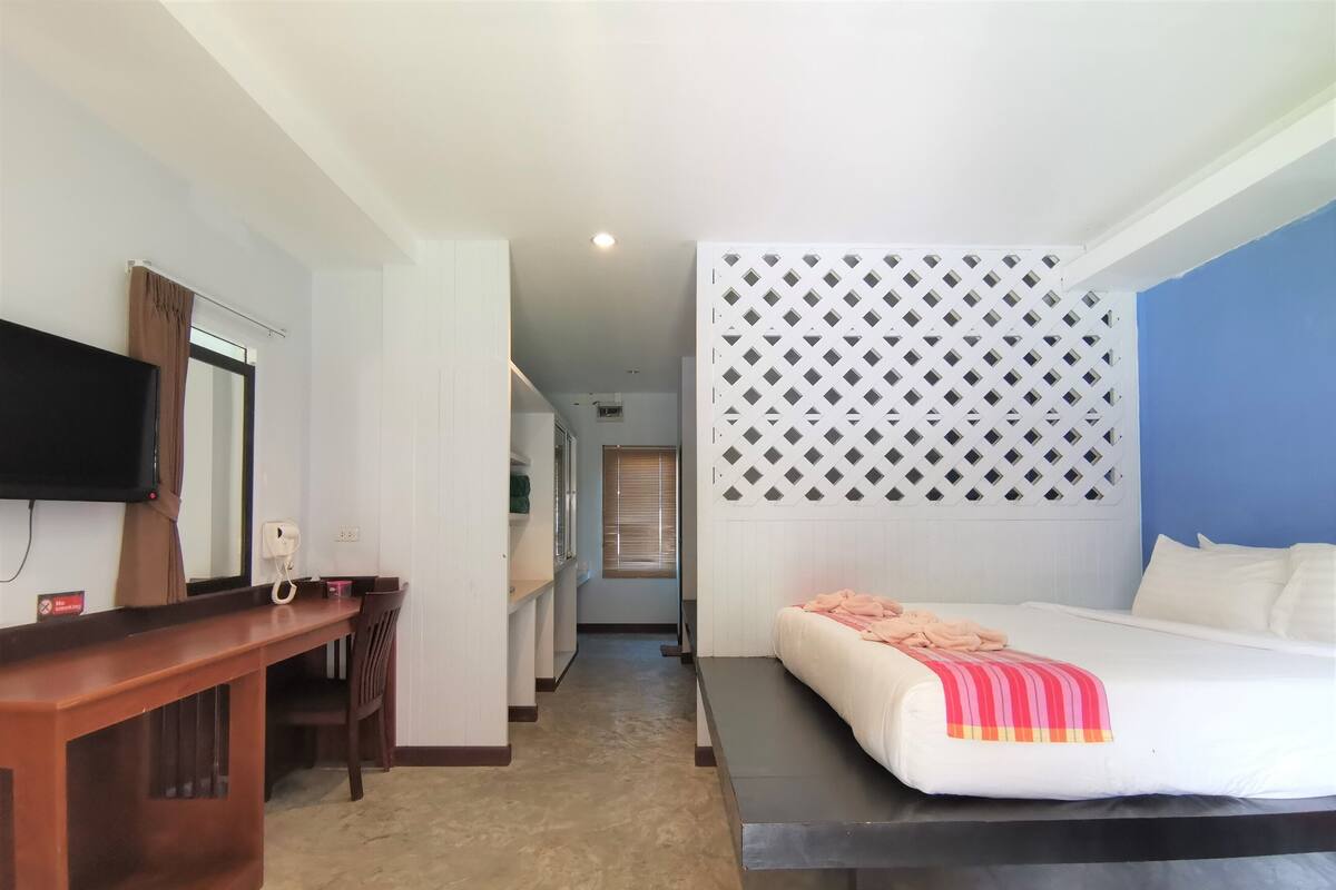 A hotel room with a bed, a desk, a TV, and a window with blinds.