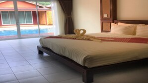 Een hotelkamer met een groot bed, uitzicht op een zwembad en een schuifdeur naar een buitengebied.