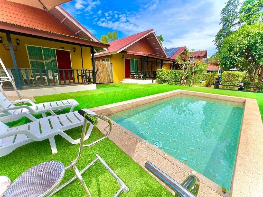A pool area with lounge chairs and a small table, surrounded by a well-maintained lawn and a building with a red roof.