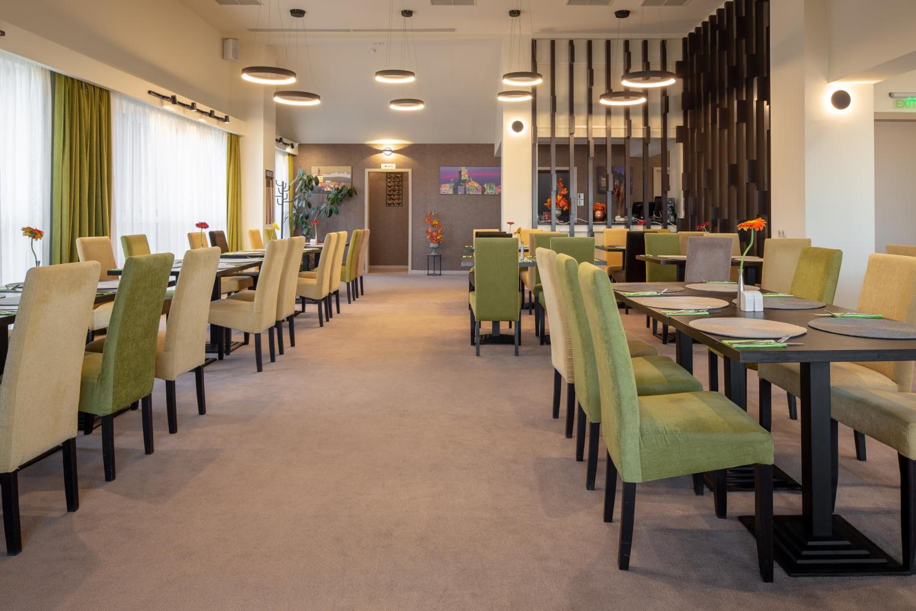 Un'ampia sala da pranzo d'albergo con numerosi tavoli e sedie, un percorso centrale e un design moderno.
