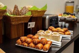 Un bufé con diversas opciones de panadería, incluyendo cruasanes y pasteles, además de una selección de panes y sándwiches.