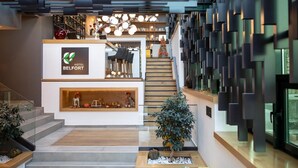 Un moderno vestíbulo de hotel con un mostrador de recepción, una escalera y una pared decorativa con motivos geométricos.