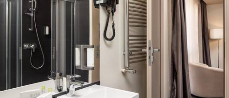 Un baño moderno con un lavabo blanco grande, una ducha con cerramiento de vidrio y un secador de pelo fijado a la pared.