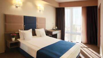 Een hotelkamer met een groot bed, een bureau, twee bedlampjes, een nachtkastje en een raam met gordijnen.