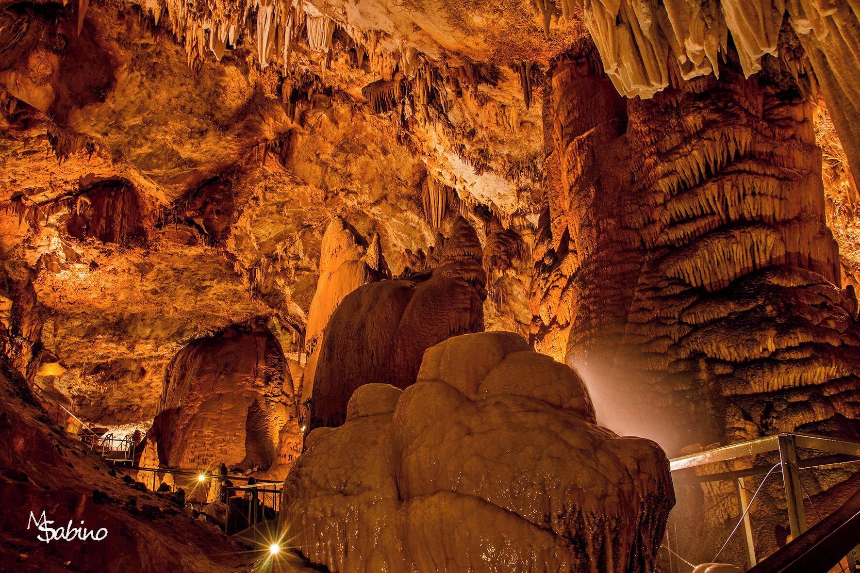 Una cueva con estalactitas y estalagmitas, un pasillo de metal y una gran formación rocosa.