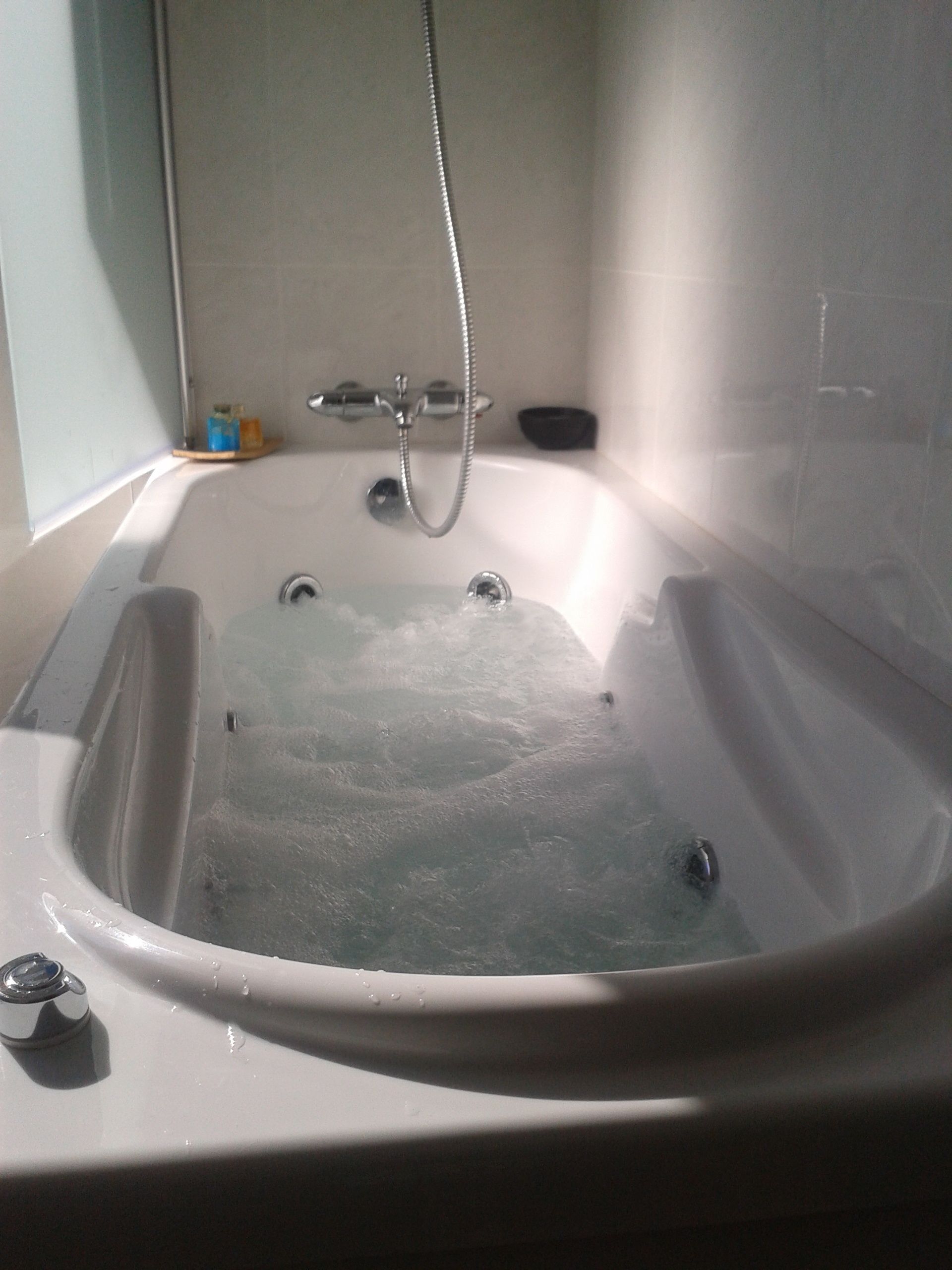A bathtub with running water, a showerhead, and a soap dish on a shelf.