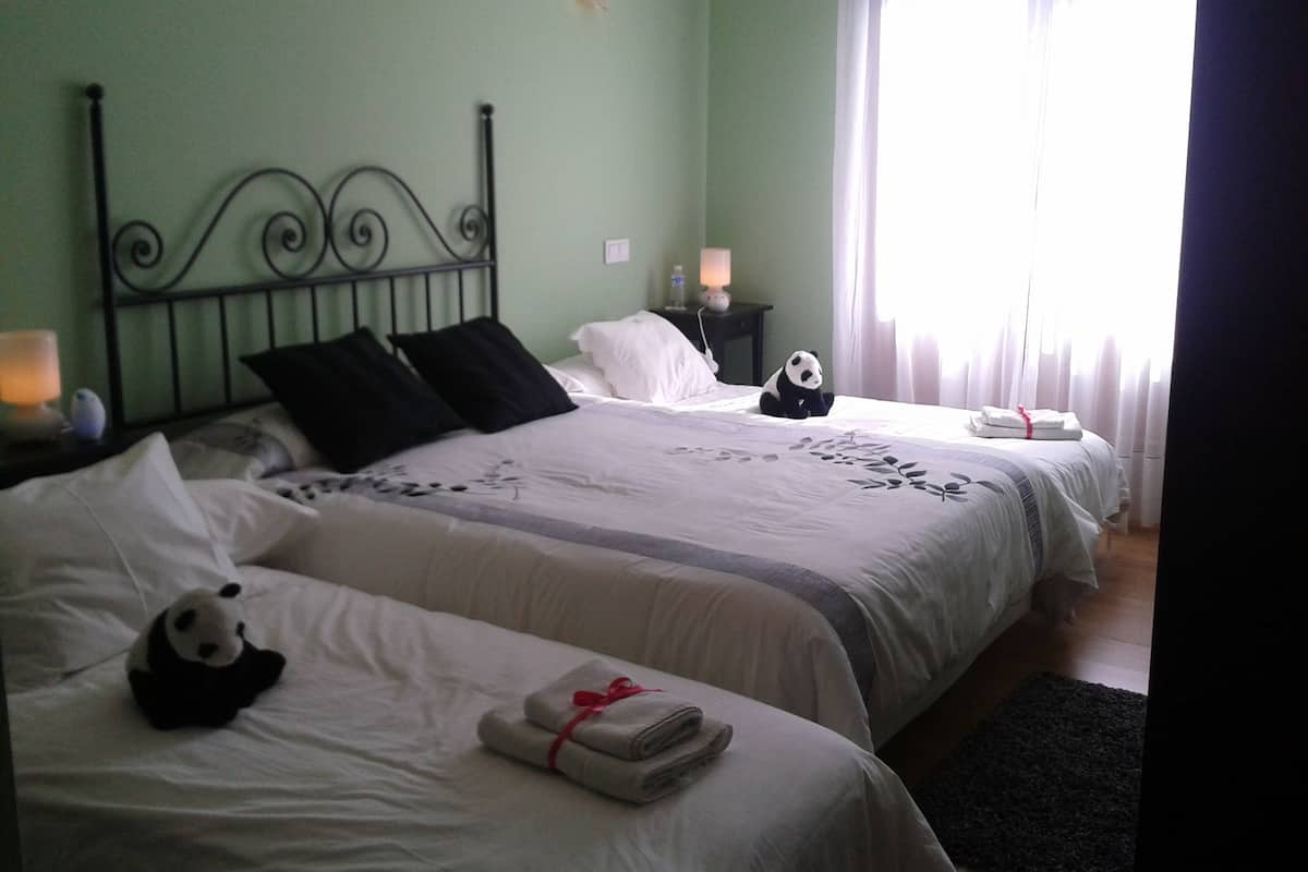Een hotelkamer met twee bedden, een nachtkastje met een lamp, een panda knuffel en een raam met gordijnen.