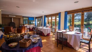 Een restaurant met meerdere tafels, een houtkachel en grote ramen met gordijnen.