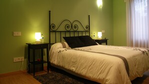 Een opgemaakt bed in een kamer met groene wanden, twee bedlampen en een raam met gordijnen.