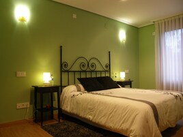 Una cama bien tendida en una habitación con paredes verdes, dos lámparas de noche y una ventana con cortinas.