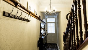 A hallway with a coat rack, a chandelier, a door with a window, and a staircase with wooden balusters.