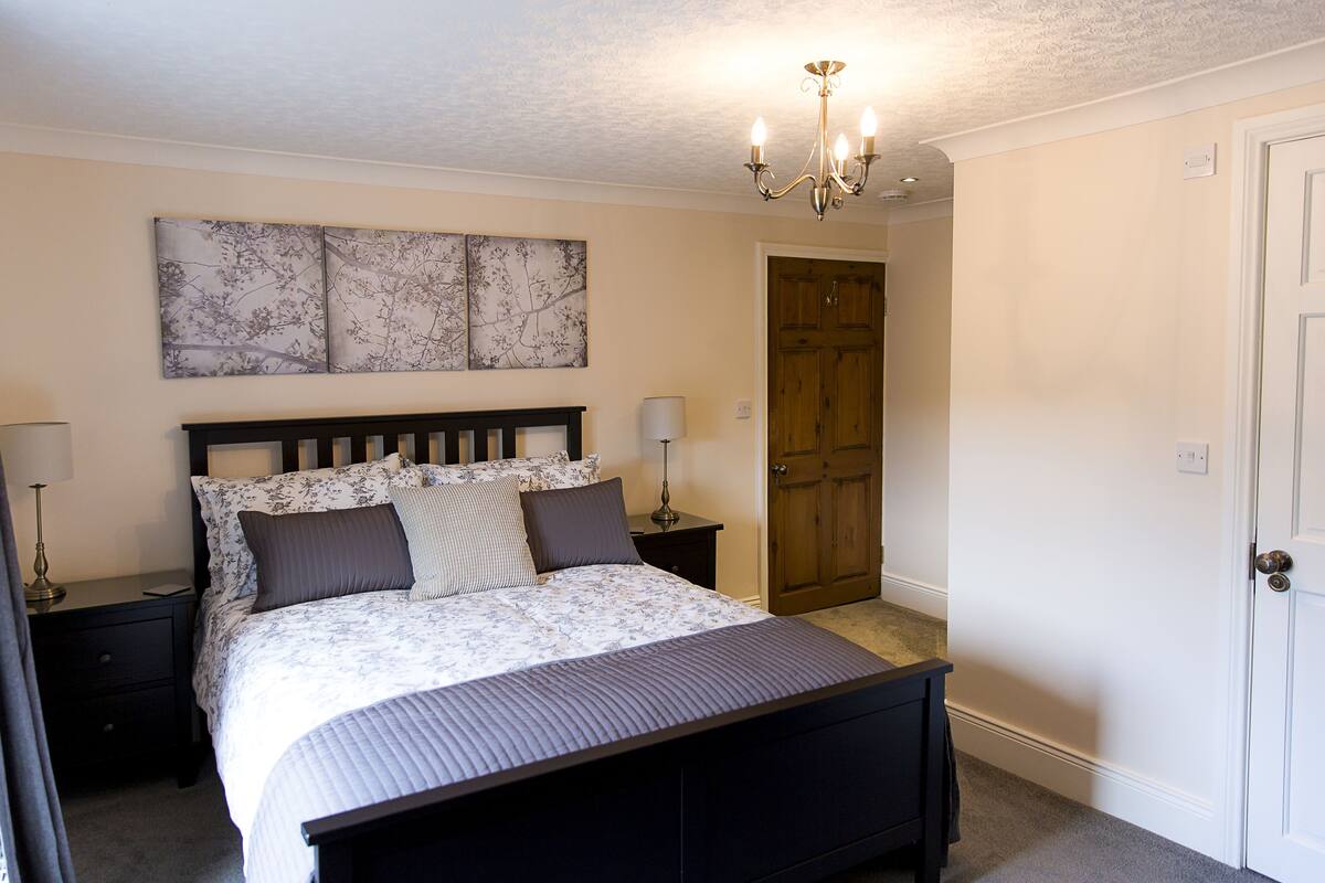 A bedroom with a bed, nightstands, a chandelier, and a door.