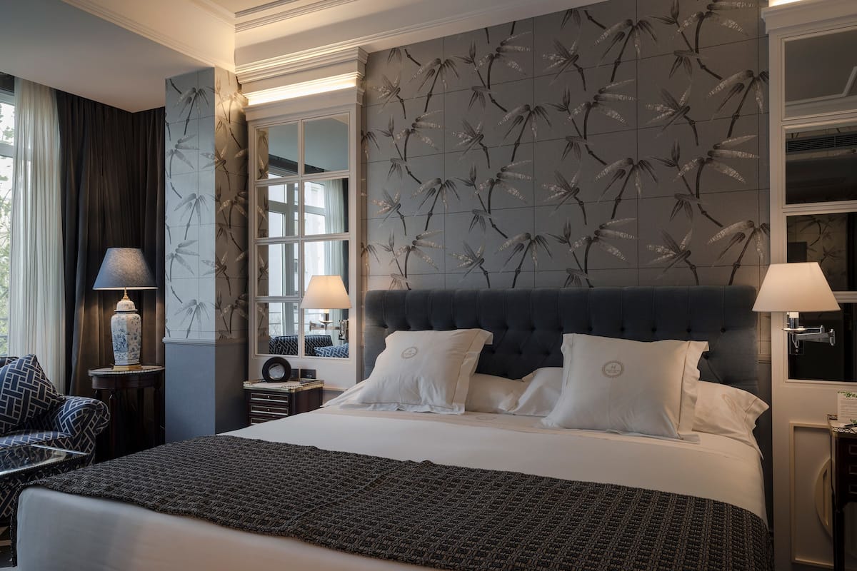 Een hotelkamer met een groot bed, twee nachtkastjes, een stoel en een raam met gordijnen.