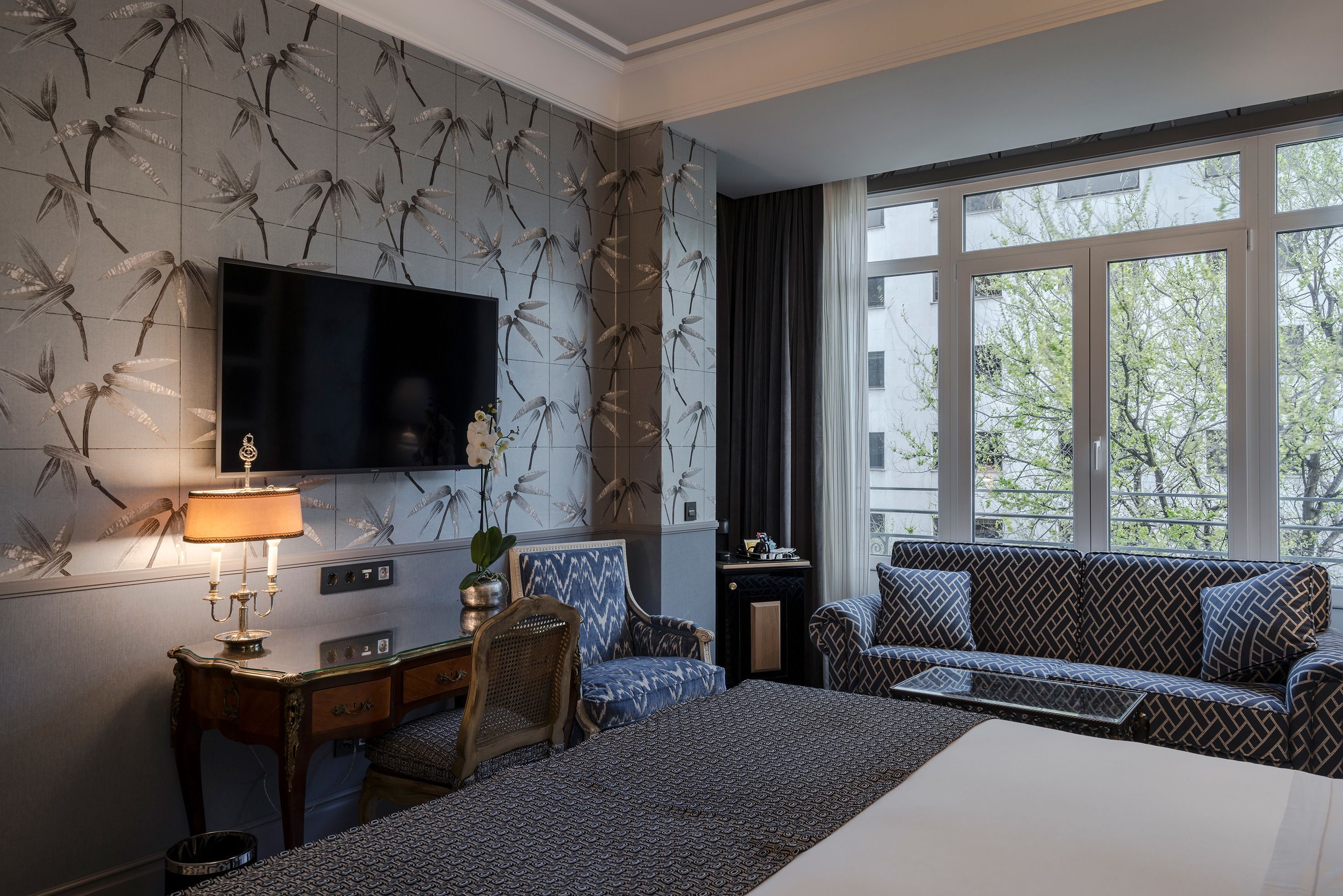 A hotel room with a large bed, a sofa, a TV, and a desk with a lamp.