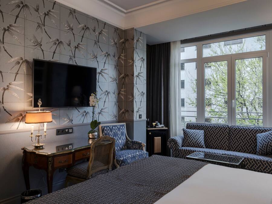 A hotel room with a large bed, a sofa, a TV, and a desk with a lamp.