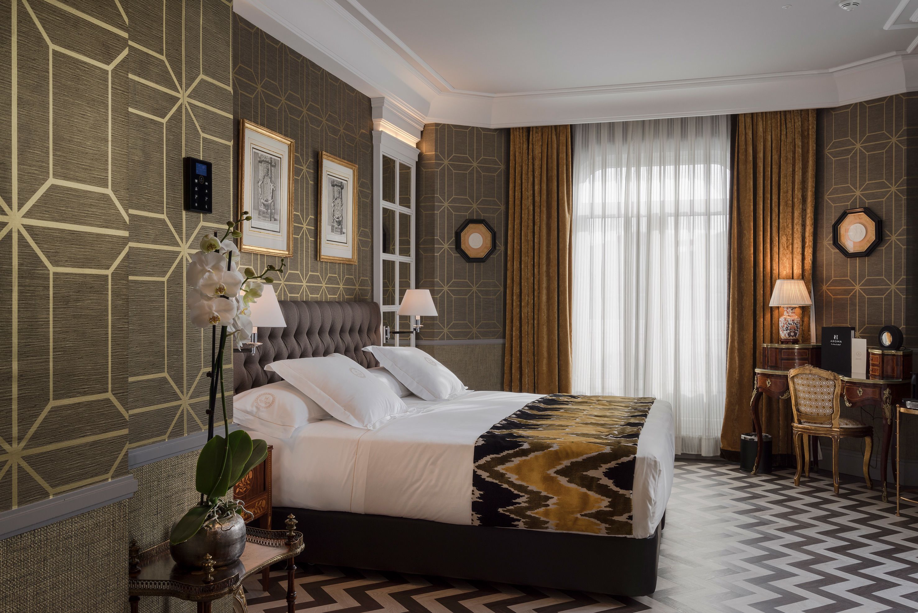 Una habitación de hotel moderna con una cama grande, un escritorio y una silla. Hay dos cuadros en la pared, una planta en maceta y una ventana con cortinas.
