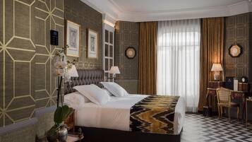 Una habitación de hotel moderna con una cama grande, un escritorio y una silla. Hay dos cuadros en la pared, una planta en maceta y una ventana con cortinas.