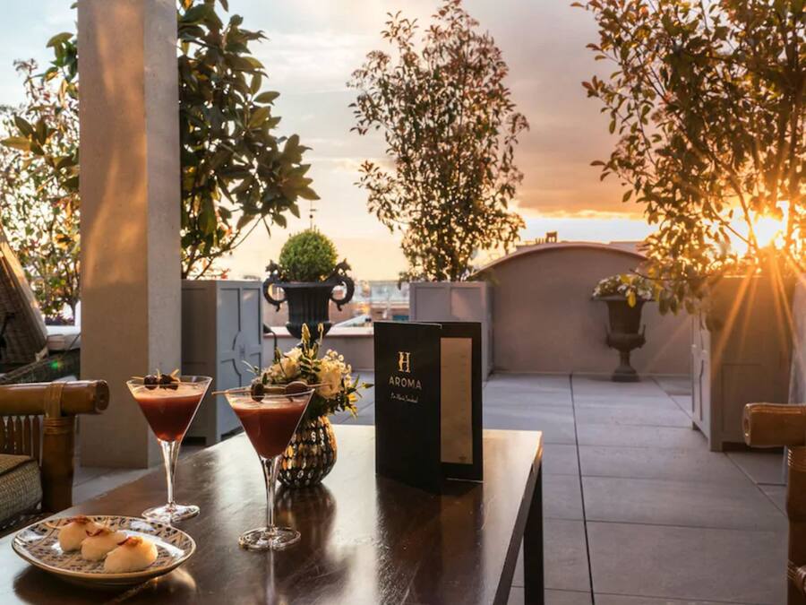 A rooftop terrace with a table set for a meal, featuring a dessert plate, two drinks, and a menu.