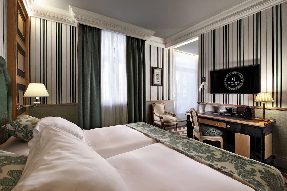 Een hotelkamer met een groot bed, een bureau, een stoel, een televisie en een raam met gordijnen.