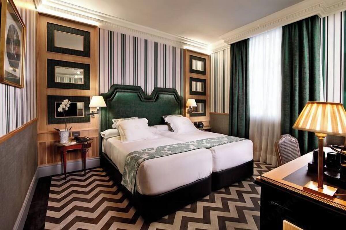 Een hotelkamer met een groot bed, twee nachtkastjes, een bureau met een lamp en een stoel.