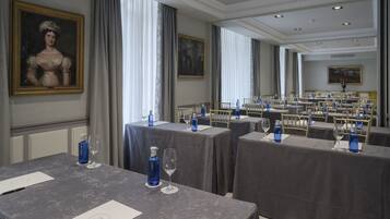 Un comedor formal con mesas dispuestas para una comida, destacando botellas de agua azules y copas de vino.