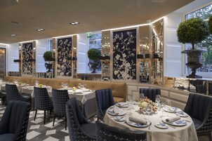 Un ristorante con tavoli rotondi, sedie imbottite blu e una parete decorativa con motivi floreali.