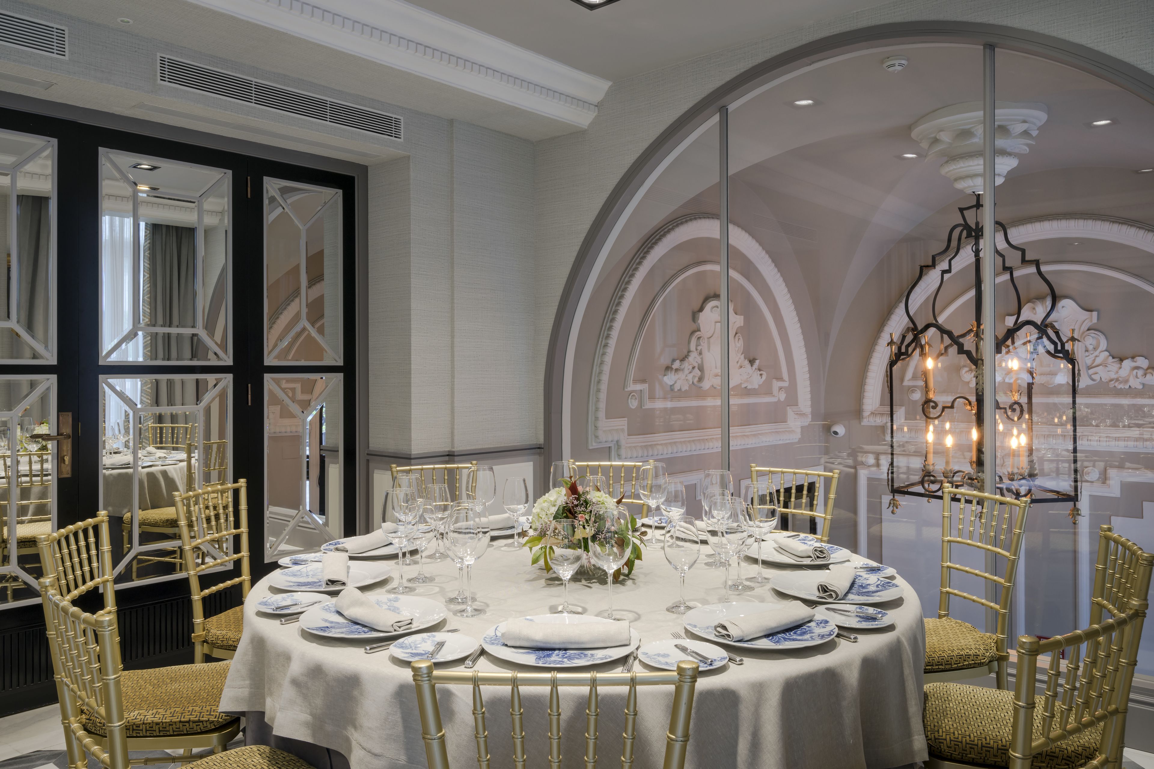 A formal dining room with round tables, gold chairs, and a chandelier.