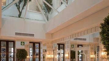 Ein geräumiger Salon mit einem geometrisch gemusterten Boden, einer hohen Decke mit Oberlicht und einer Sitzecke mit gemusterten Polstern.