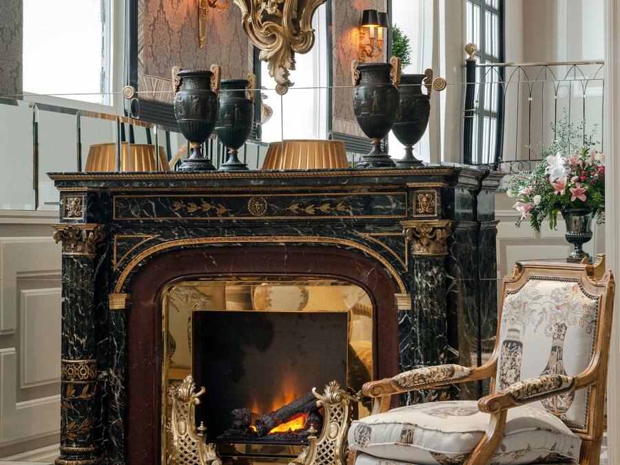 A luxurious room with a marble fireplace, ornate furniture, and a large wall clock.