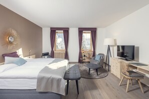 Quarto de hotel moderno com uma cama grande, uma escrivaninha com computador, uma televisão e uma cadeira.
