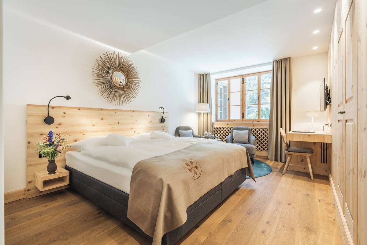 A modern bedroom with a wooden headboard, a large bed, a desk, and a window with curtains.