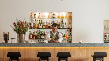 A bar area with a bartender, a chandelier, and a shelf of liquor bottles.
