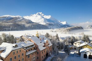 Paisagem montanhosa coberta de neve com um hotel, incluindo vários edifícios e um campanário.