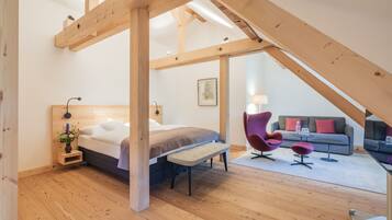 Ein Schlafzimmer mit Bett, Holzbalken, einer Bank, einem Sessel und einer Couch in einem Loft-Zimmer.