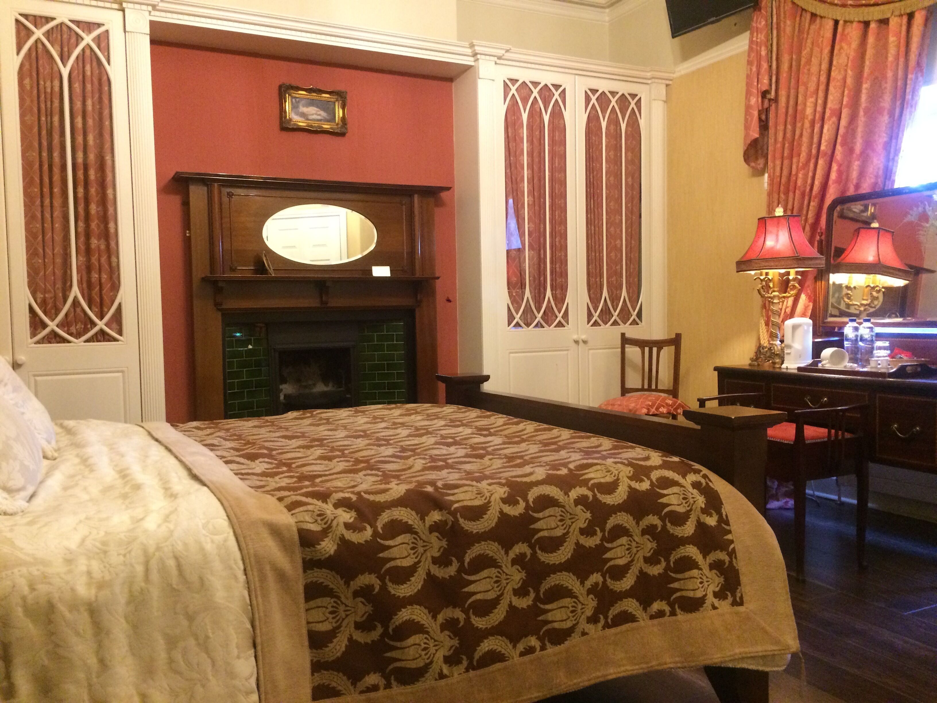 Una habitación de hotel con una cama, una chimenea, un escritorio con lámpara y un espejo.