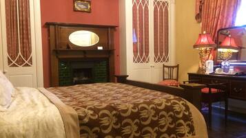 Quarto de hotel com cama, lareira, escrivaninha com candeeiro e espelho.