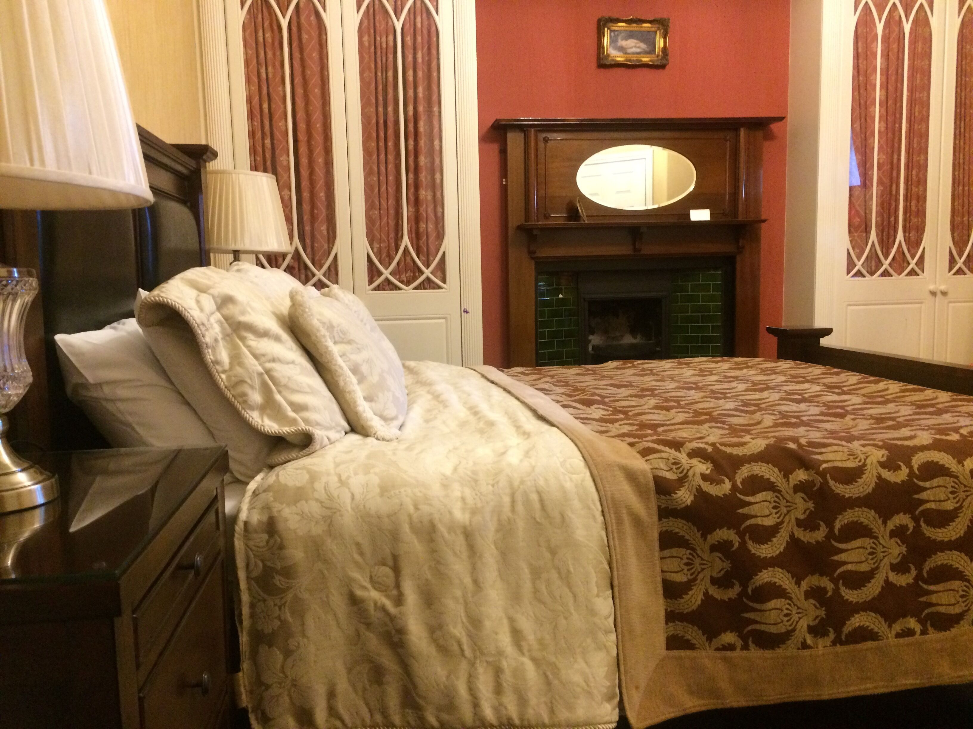 A neatly made bed with a patterned bedspread, a bedside lamp, and a dresser with drawers.