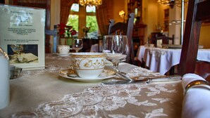 A dining table set with fine china and silverware, a menu, and a chandelier in a warmly lit room.