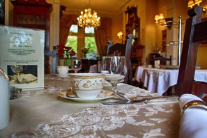 A dining table set with fine china and silverware, a menu, and a chandelier in a warmly lit room.
