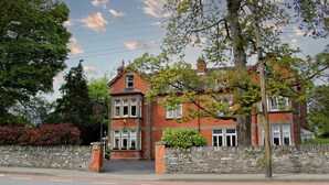 A red brick building with a stone wall, a large tree, and a clear sky. - Innisfree House (Dundalk)